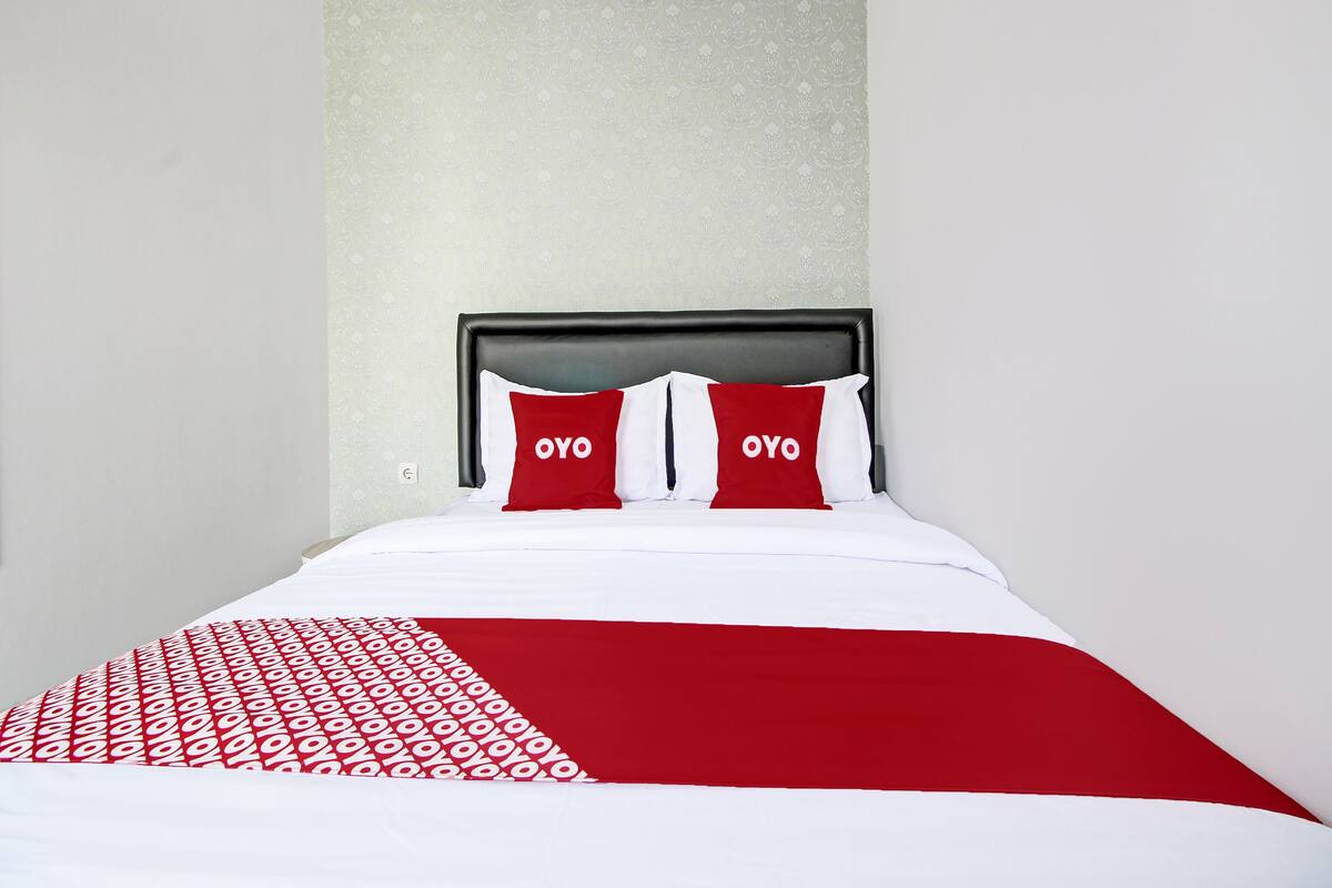 A neatly made bed with a red and white bedspread and two pillows with the word "OYO" on them.