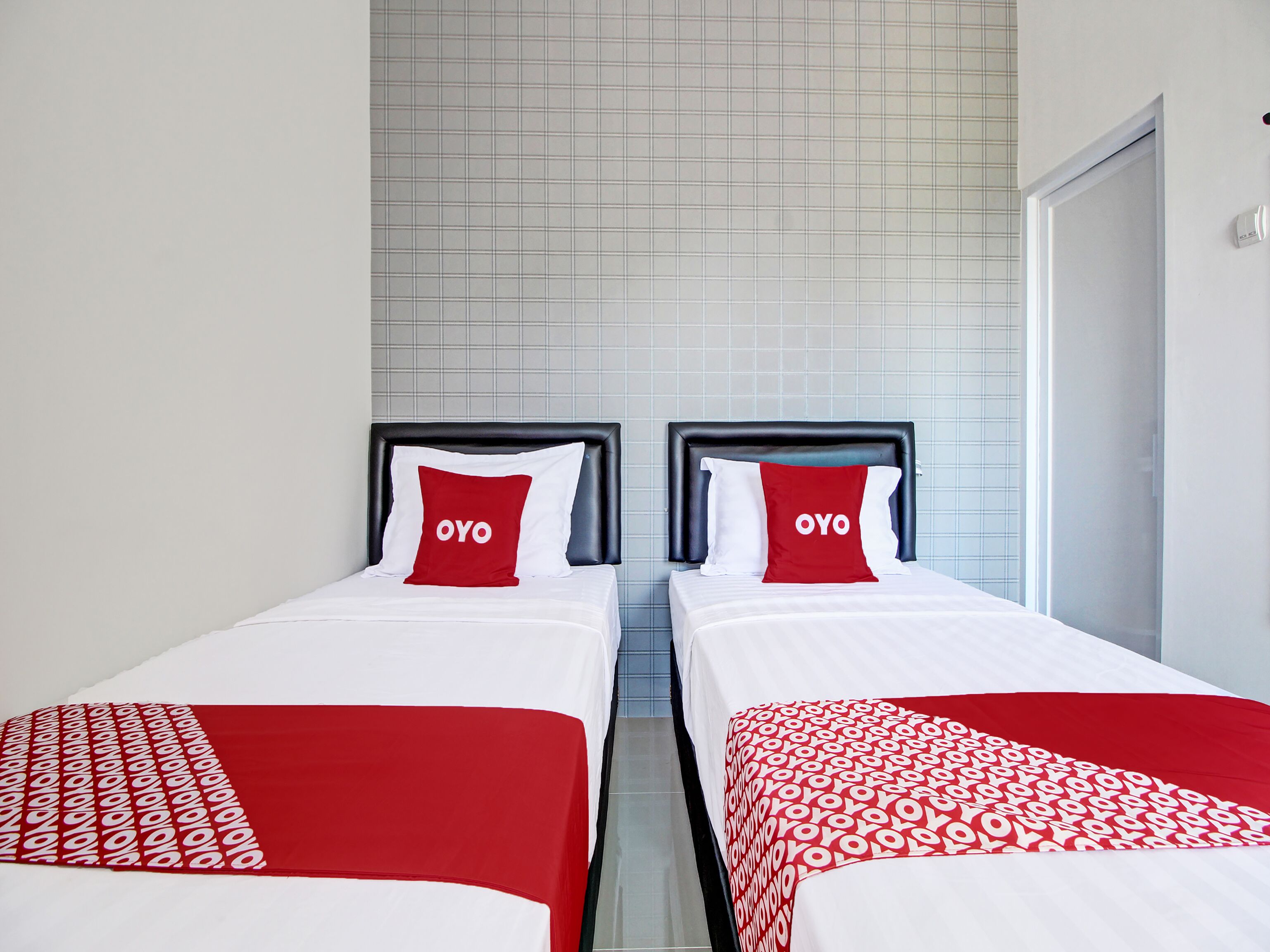Dos camas individuales con ropa de cama roja y blanca, una pared de azulejos y una puerta.