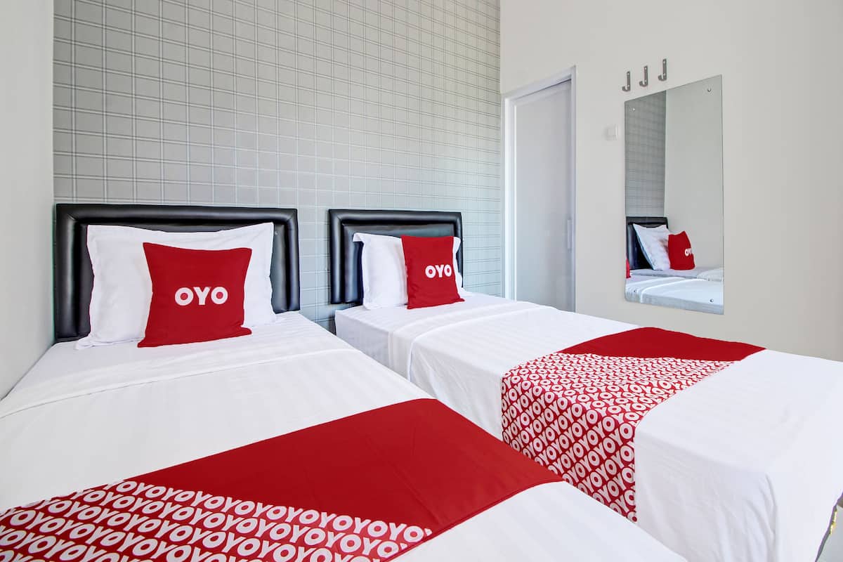 A hotel room with two beds, each with a red and white bedspread and pillows, and a large mirror on the wall.