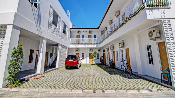 A courtyard with a red car parked in the center, surrounded by white buildings with balconies and air conditioning units.