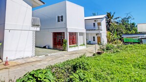A modern two-story house with a red gate, a balcony, and a small garden area.