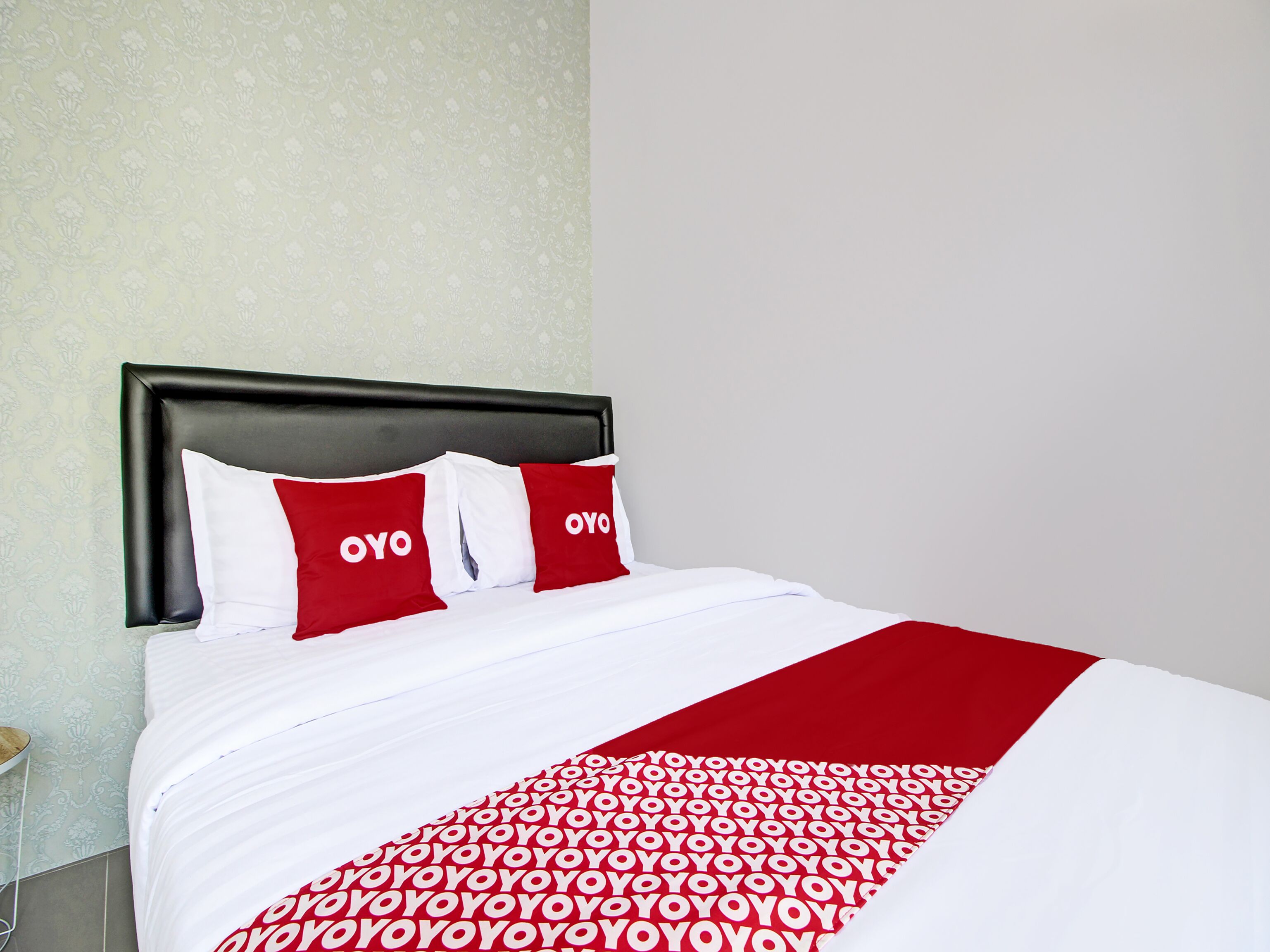 Habitación de hotel con una cama cubierta con una colcha de diseño rojo y blanco, y dos almohadas con la palabra 'OYO'.