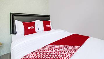 Habitación de hotel con una cama cubierta con una colcha de diseño rojo y blanco, y dos almohadas con la palabra 'OYO'.