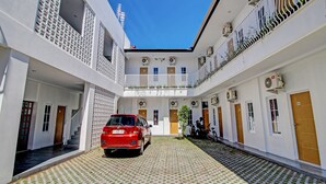 A courtyard with a red car parked in the center, surrounded by white buildings with balconies and air conditioning units.