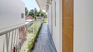 Un pasillo estrecho con piso de baldosas, una puerta de madera con la etiqueta “A4” y una barandilla blanca adornada con plantas.