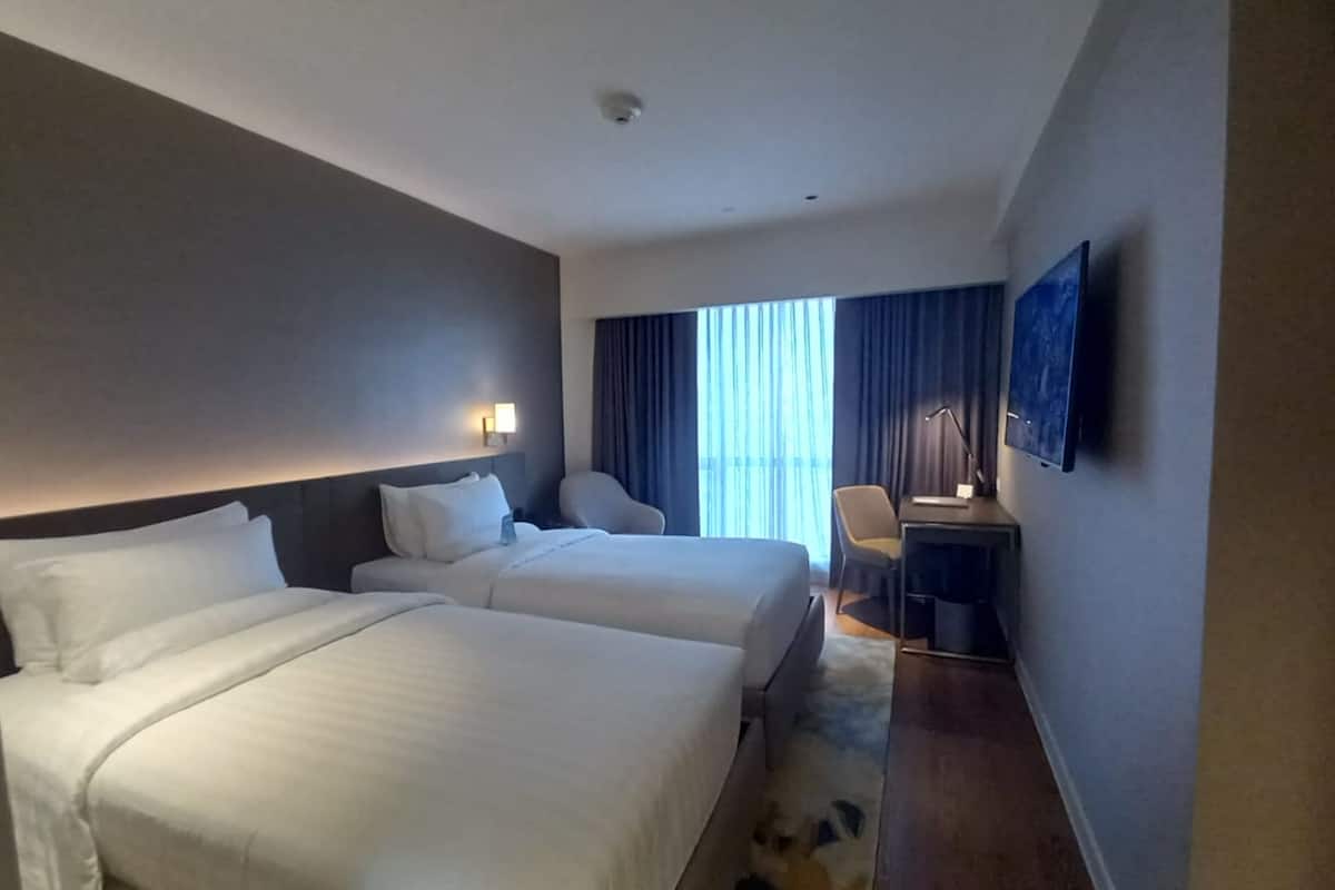 A hotel room with two beds, a desk, a chair, and a large window with curtains.