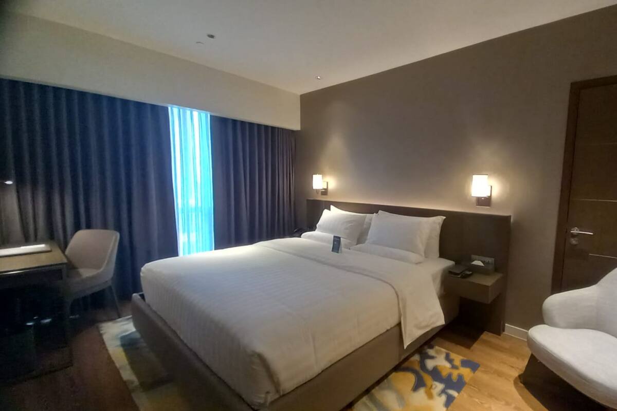 A hotel room with a large bed, a desk with a chair, a nightstand, and a chair.