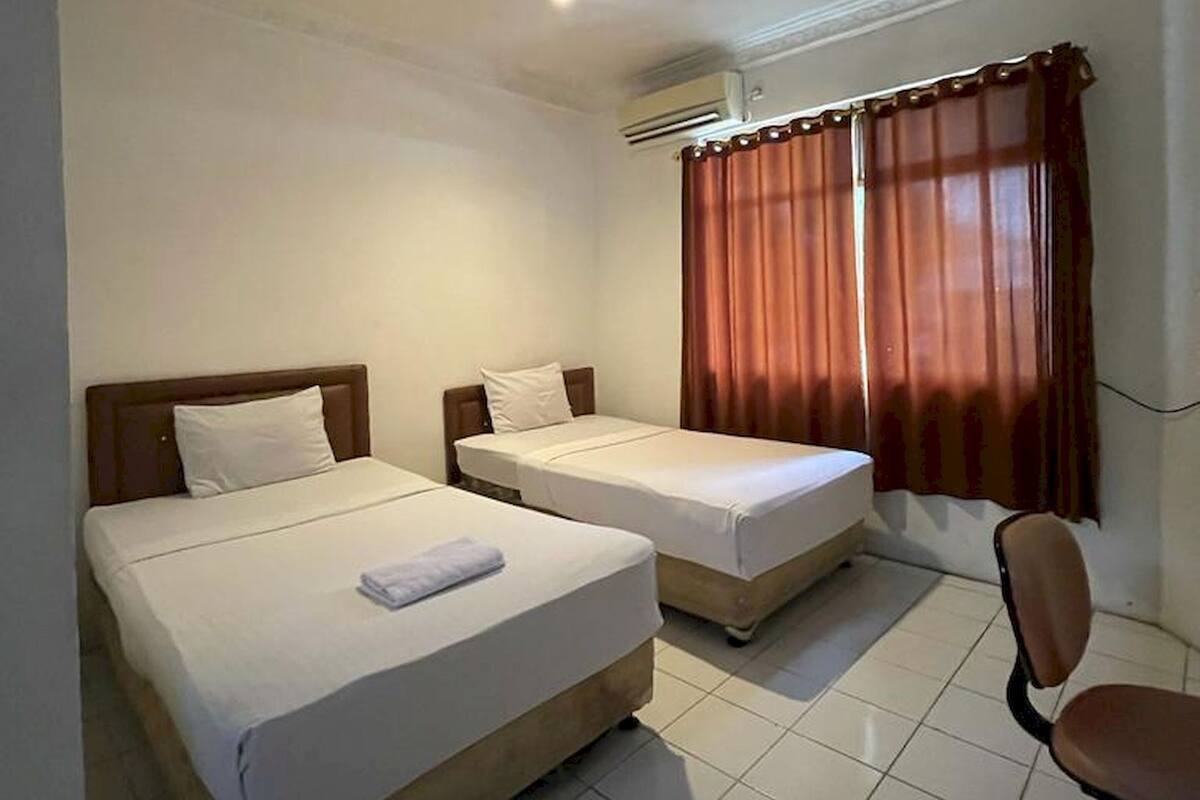 Een hotelkamer met twee bedden, een stoel, een bureau en een airconditioning.