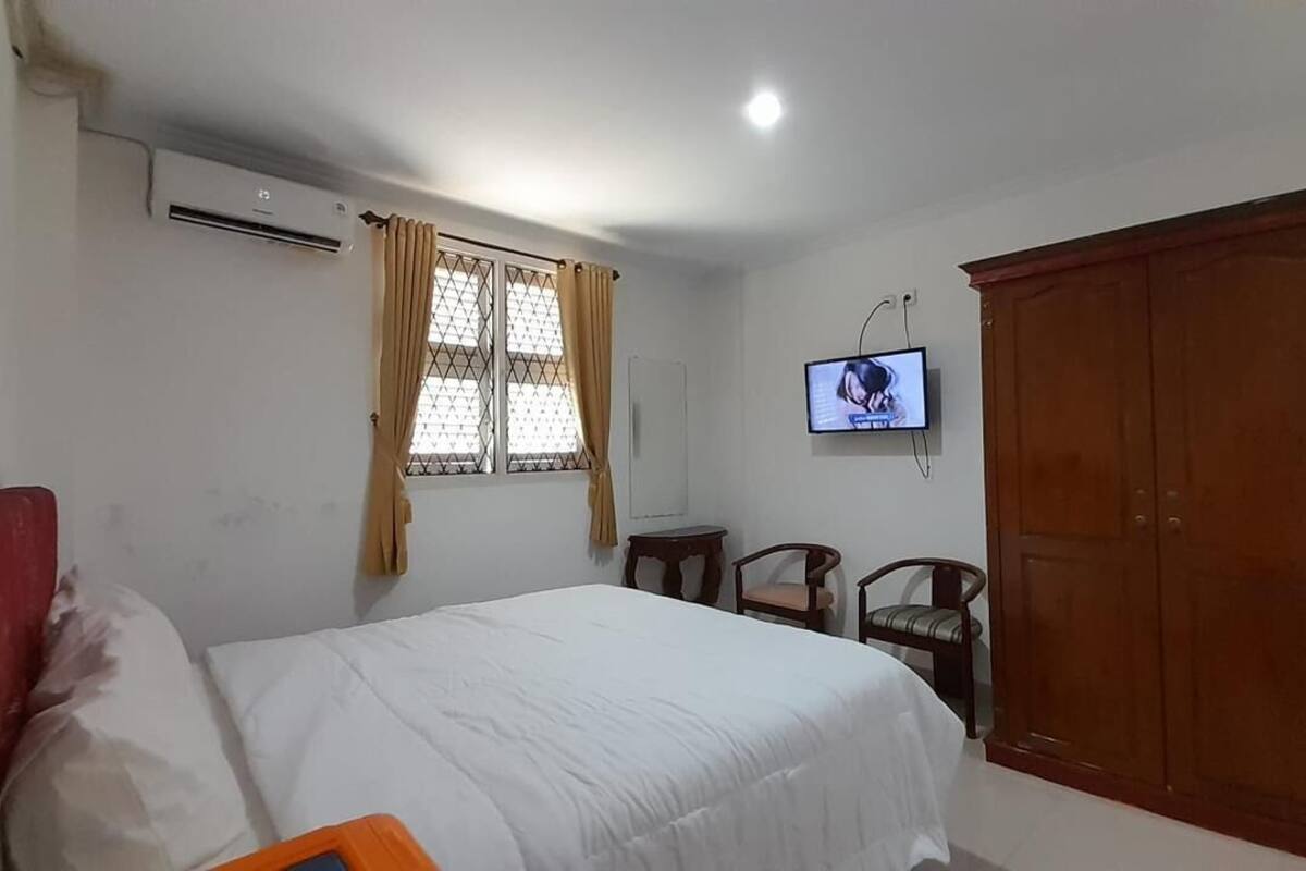 Een slaapkamer met een bed, een televisie, een kledingkast en een raam met gordijnen.