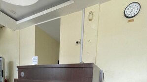 Een receptiebalie met een klok aan de muur, een bruine leren bank en een deur met een brievenluik.