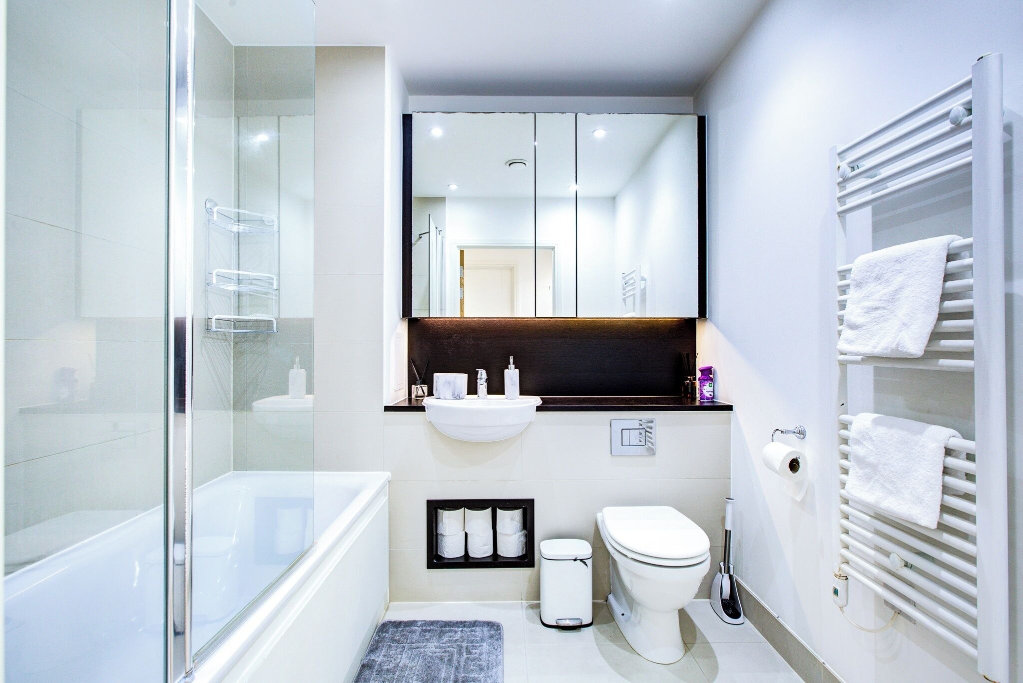 Un baño moderno con cabina de ducha de vidrio, un lavabo blanco, un inodoro y un perchero para toallas.