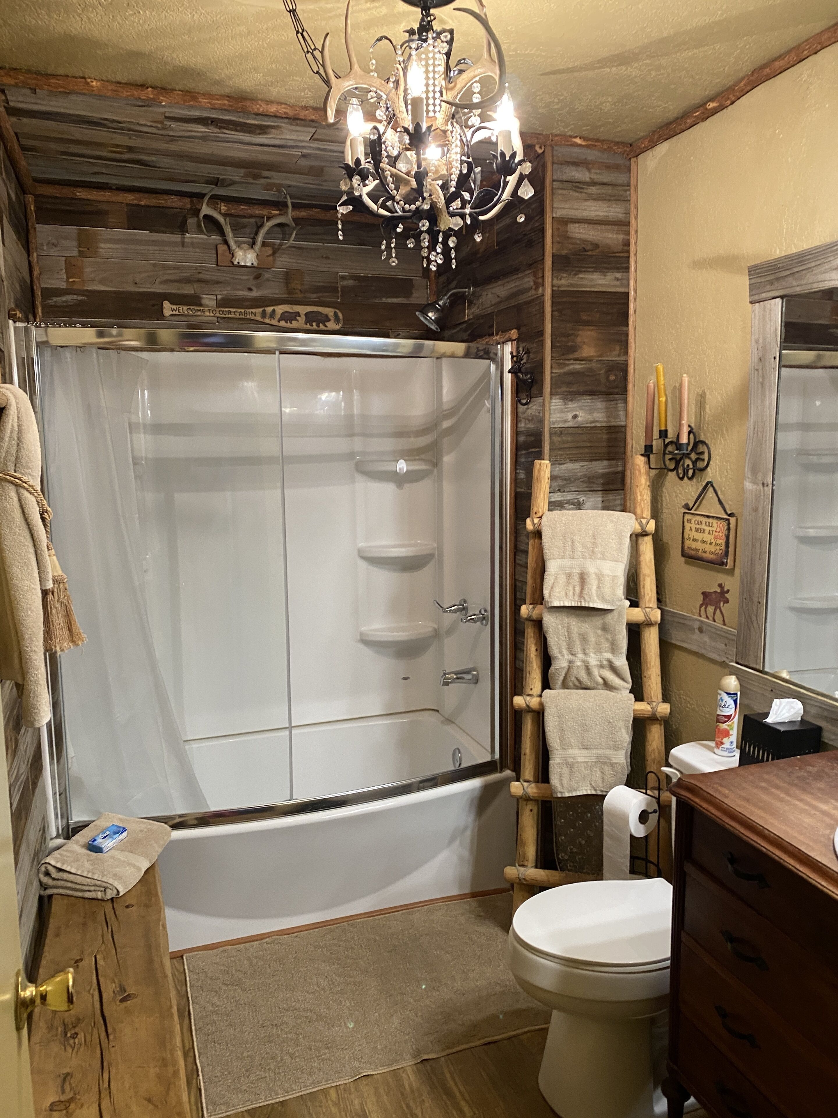 A rustic cabin bathroom with a shower, toilet, and wooden vanity.