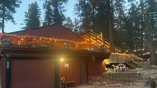 A rustic building with a wooden deck and string lights, surrounded by trees.