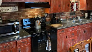 A kitchen with wooden cabinets, a brick backsplash, a microwave, an oven, and a sink.