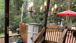 A wooden deck with a glass table and chairs, surrounded by a railing and a red umbrella.