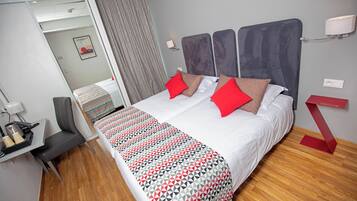 Une chambre d’hôtel avec un grand lit, un bureau avec une chaise, un miroir et un mur d’accent de couleur rouge.