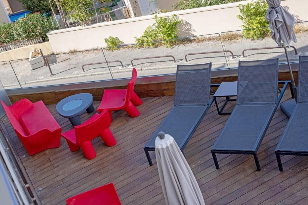 Une terrasse avec des chaises longues, des chaises rouges et une petite table.