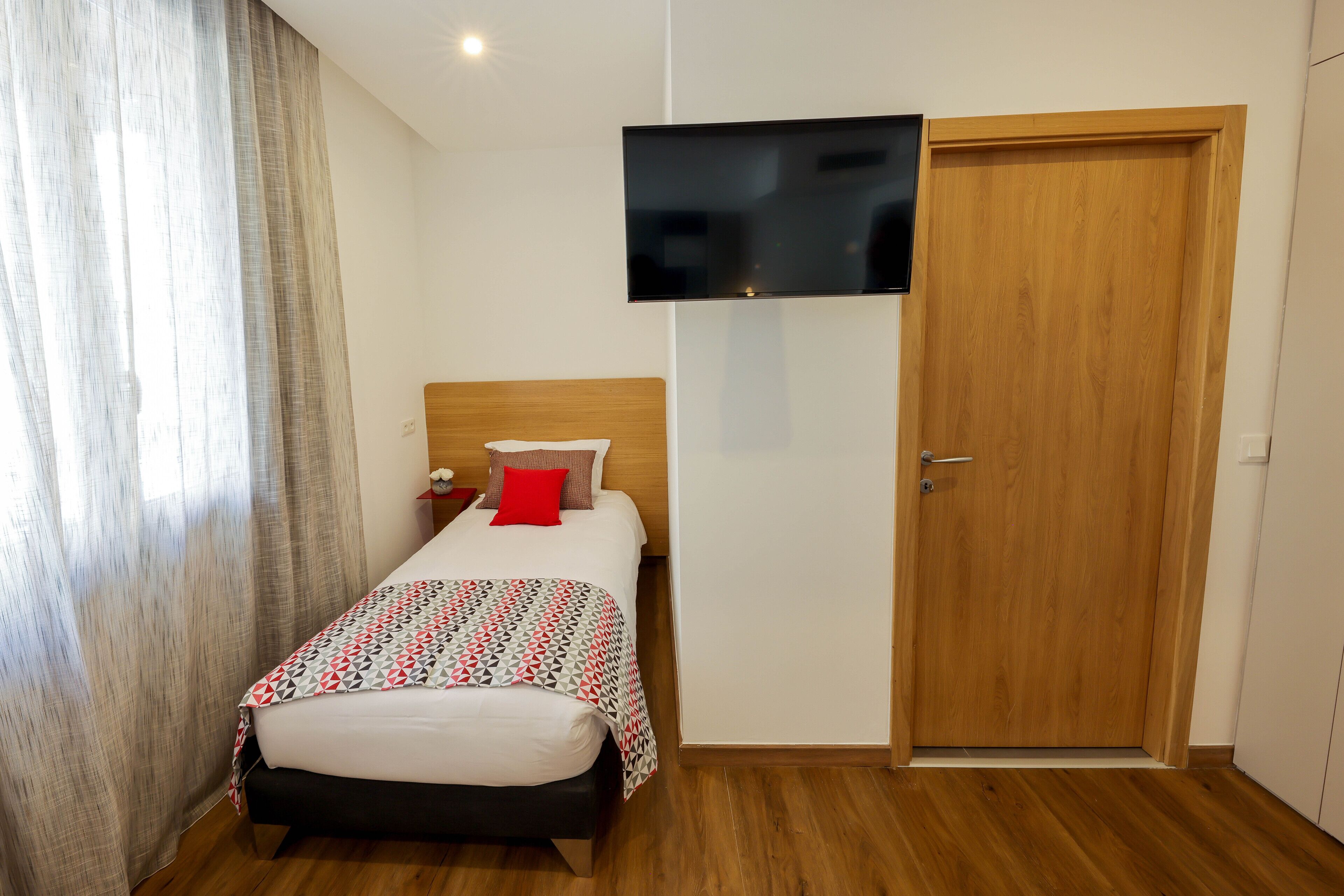 A hotel room with a bed, a television mounted on the wall, and a wooden door.