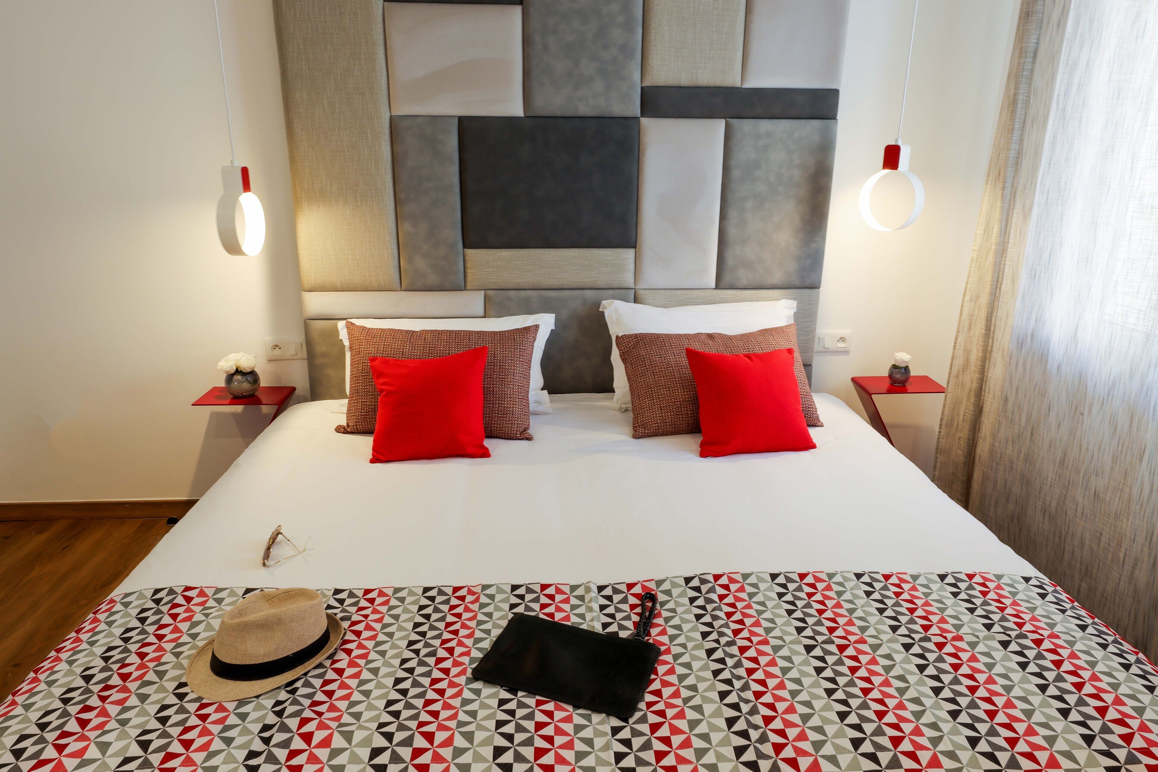 A neatly made bed with a geometric-patterned bedspread, two red pillows, and a black bag on the bed.