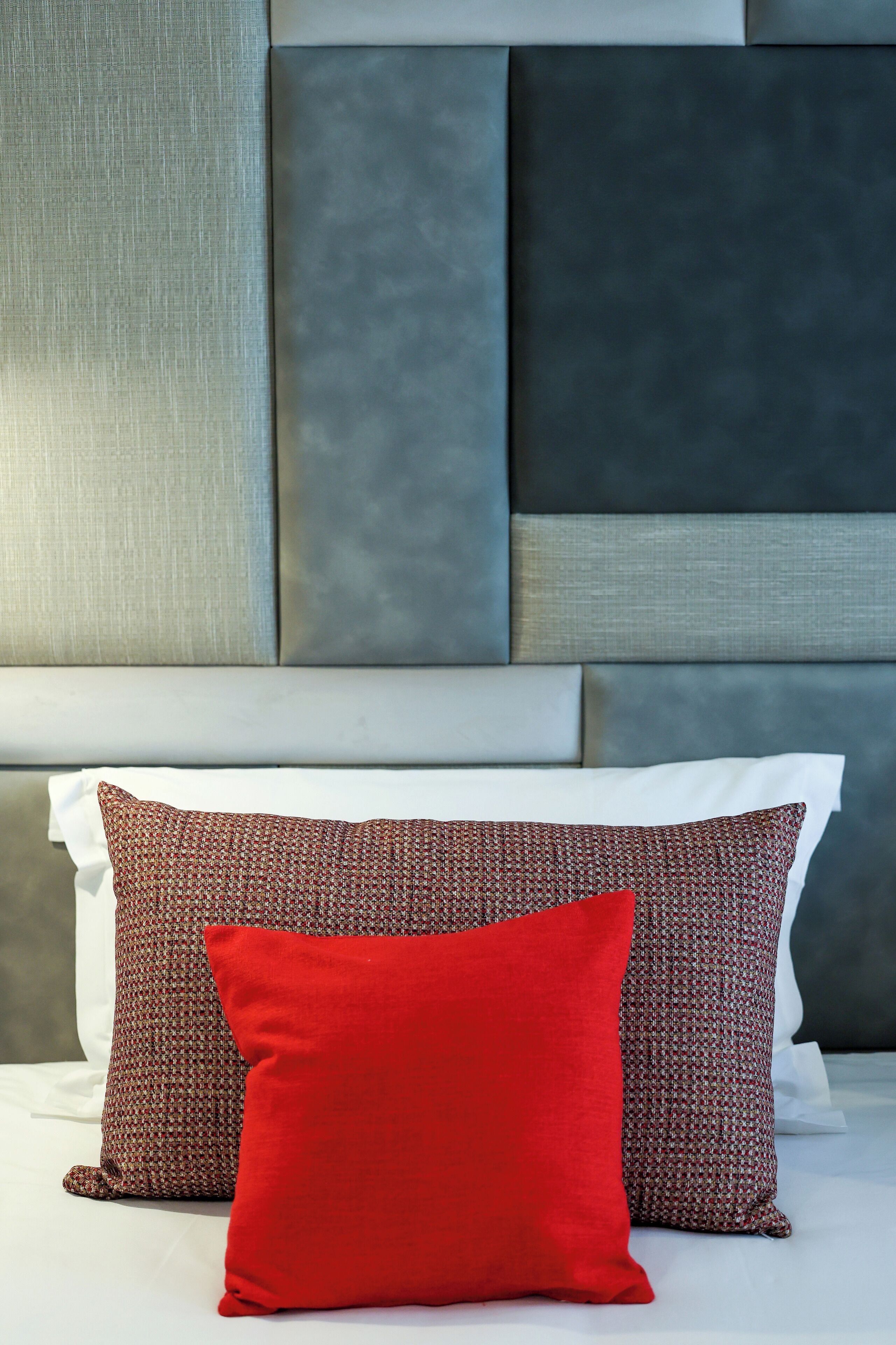 A bed with two pillows, one red and one patterned, against a headboard with a textured design.