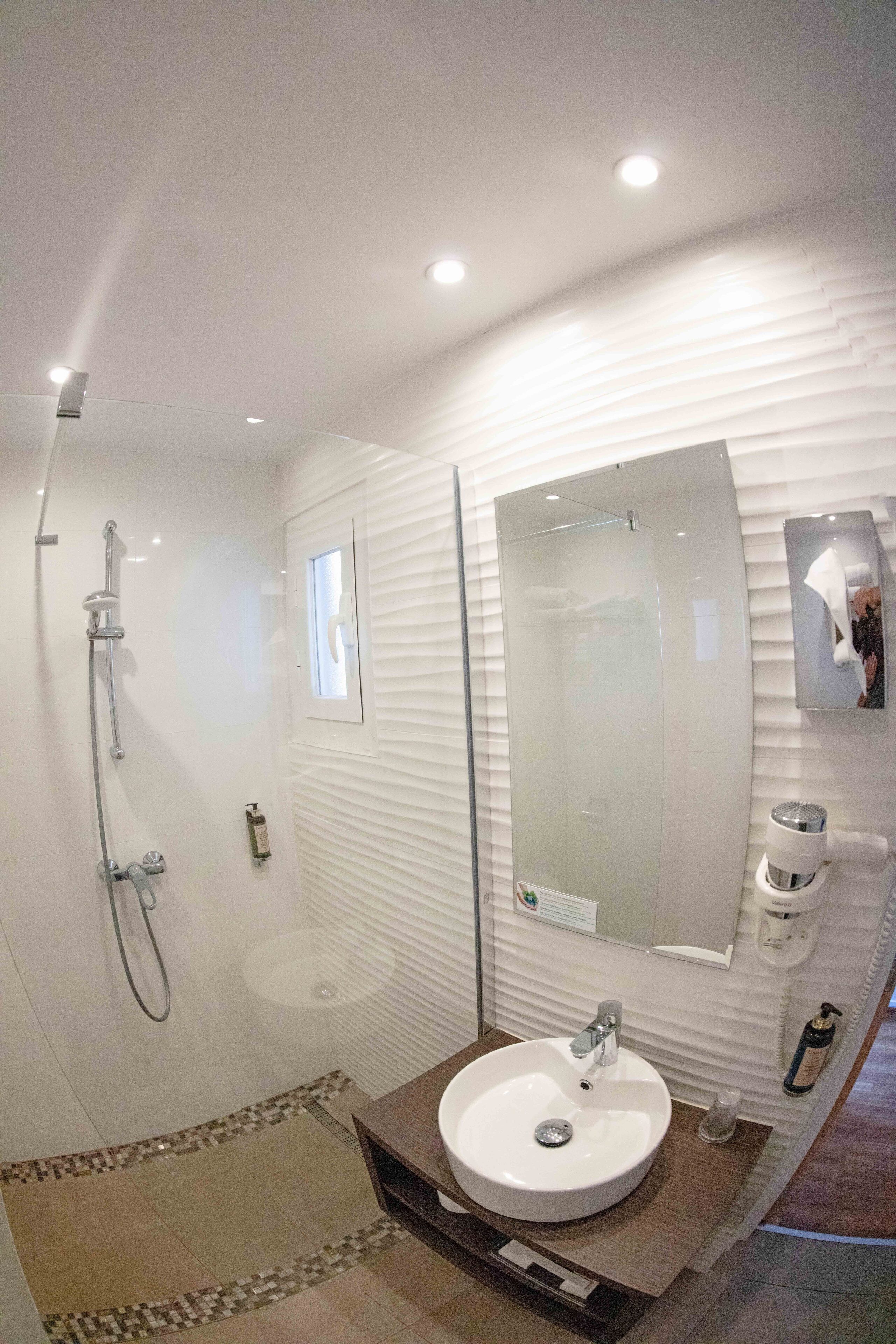 Une salle de bain moderne dotée d’une douche à parois de verre, d’un grand miroir et d’un lavabo avec un plan de travail en bois.