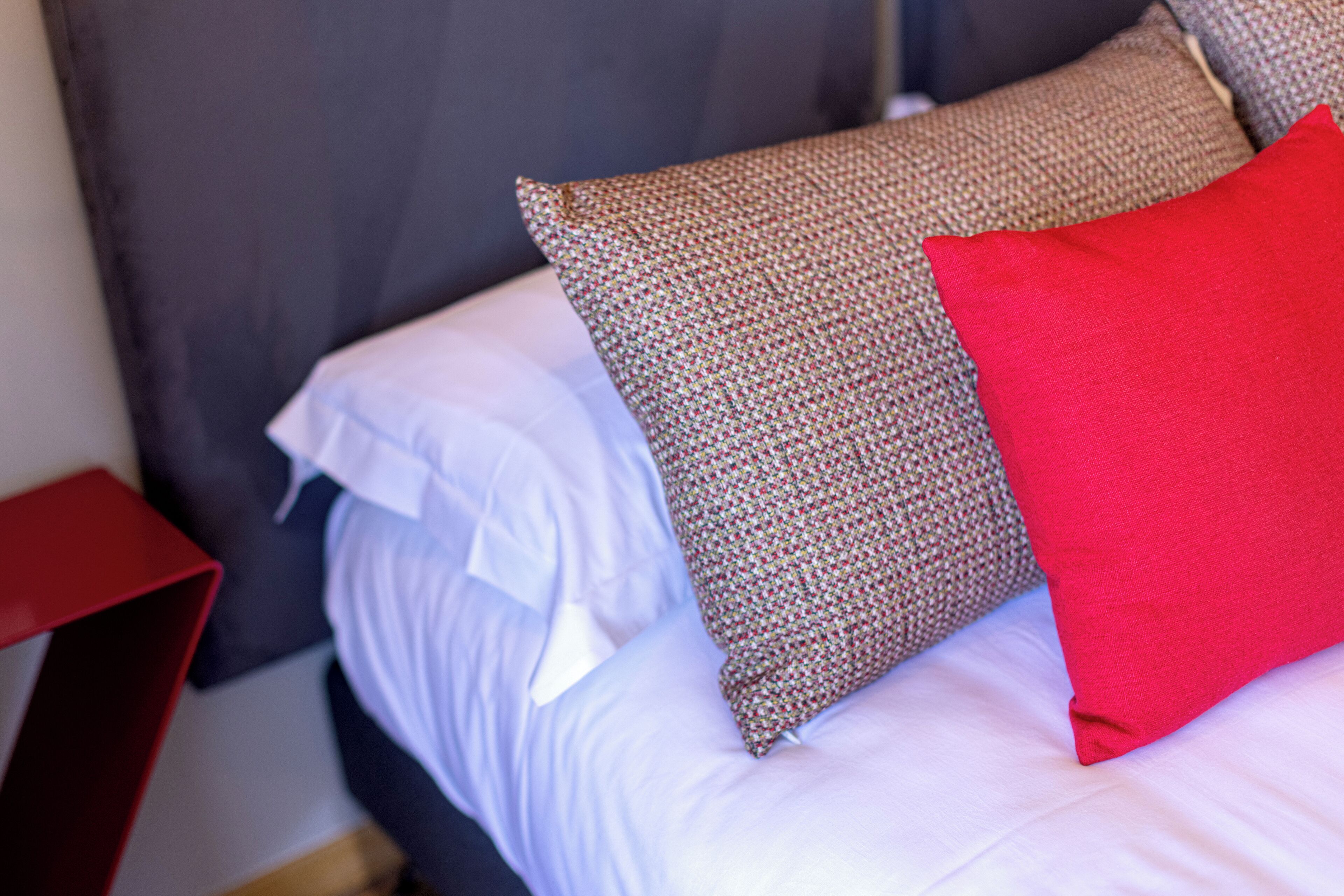 A bed with white and brown pillows, a red pillow, and a dark headboard.
