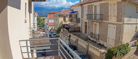 A balcony with outdoor furniture, a view of a street with buildings, and a clear blue sky.
