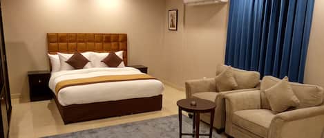 Una habitación de hotel con una cama grande, un sofá, una mesita y un aire acondicionado.