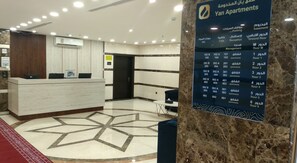Un espace d’accueil doté d’un sol en marbre, d’un comptoir de réception et d’un panneau indiquant les numéros des appartements et les étages correspondants.