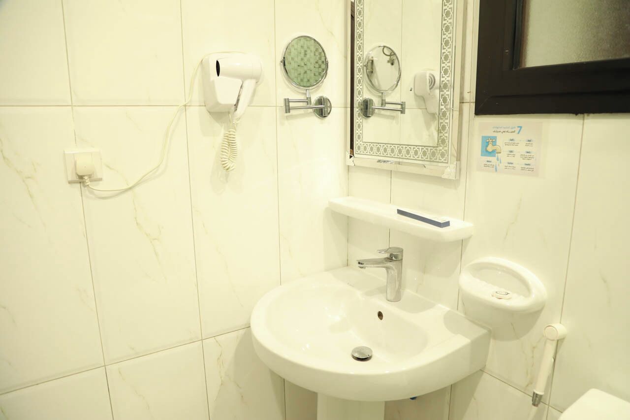 Un baño con un lavamanos blanco, un espejo, un cabezal de ducha de mano y un inodoro.