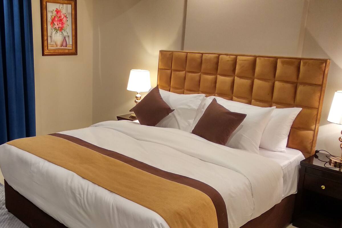 Ein Hotelzimmer mit einem großen Bett, zwei Nachttischen mit Lampen, einem blauen Vorhang und einem gerahmten Bild an der Wand.