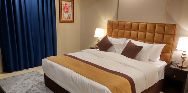 Une chambre d’hôtel avec un grand lit, deux tables de chevet avec des lampes, un rideau bleu et un tableau encadré au mur.