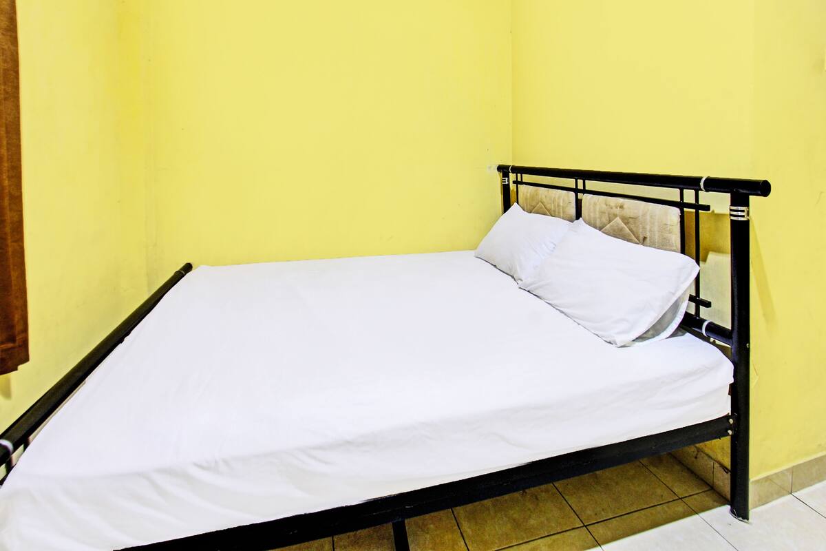 Un lit simple avec un matelas et des oreillers blancs, dans une pièce aux murs jaunes.