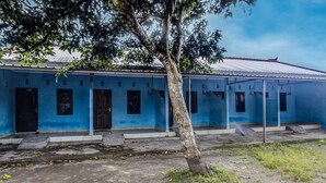 A blue building with multiple doors and windows, a tree in front, and a concrete ground with scattered leaves. - Hotel O Kos Agi Mataram Near Masjid Hissoh Al-Faham (Mataram)