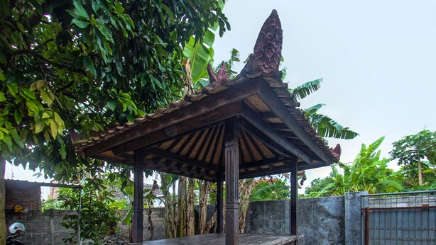 A gazebo with a tiled base and a wooden roof, surrounded by greenery and a brick wall. - Hotel O Kos Agi Mataram Near Masjid Hissoh Al-Faham (Mataram)