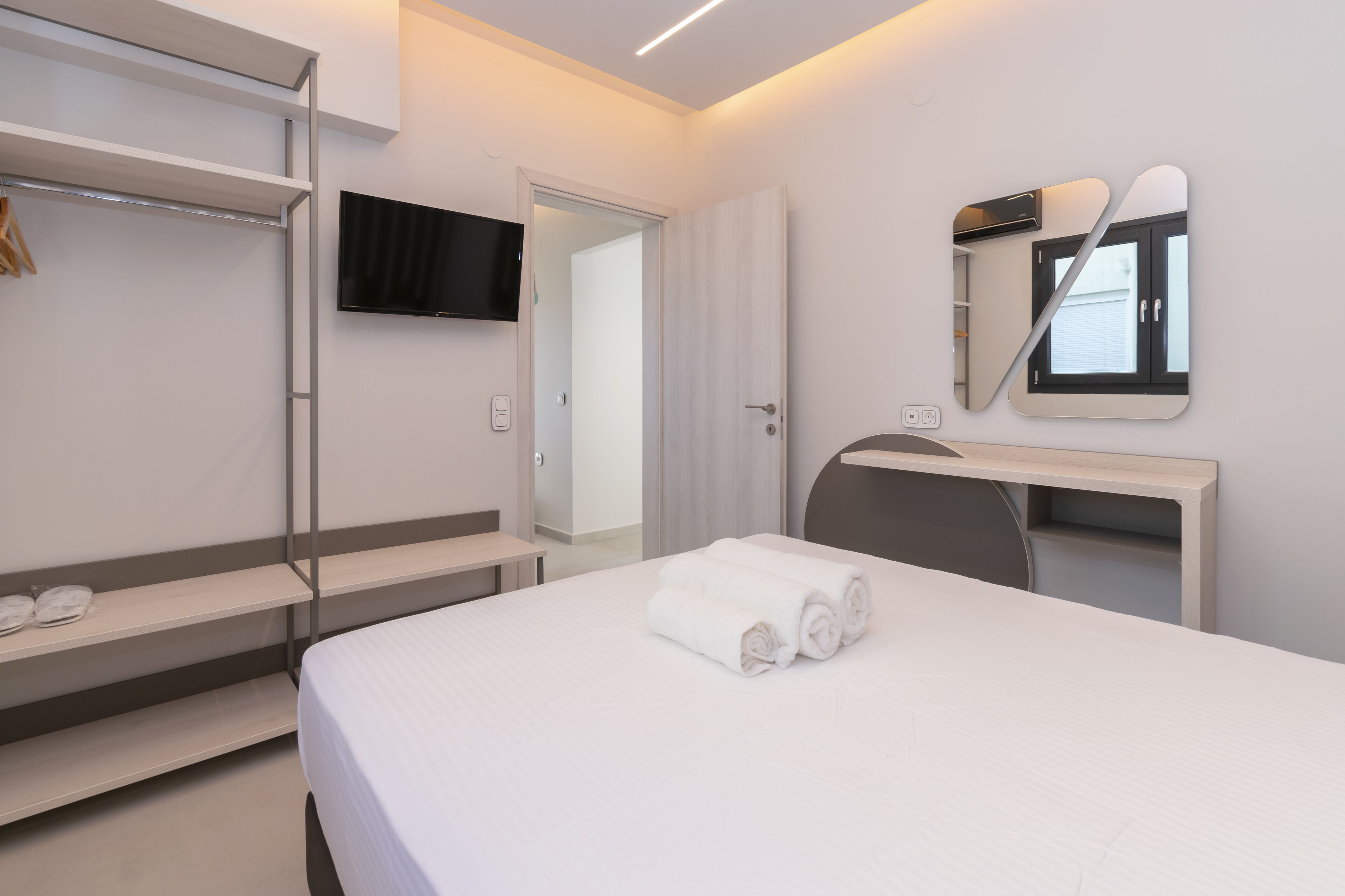 Et moderne hotelværelse med en seng, et fjernsyn ophængt på væggen, et skrivebord med stol og en garderobe med spejl.