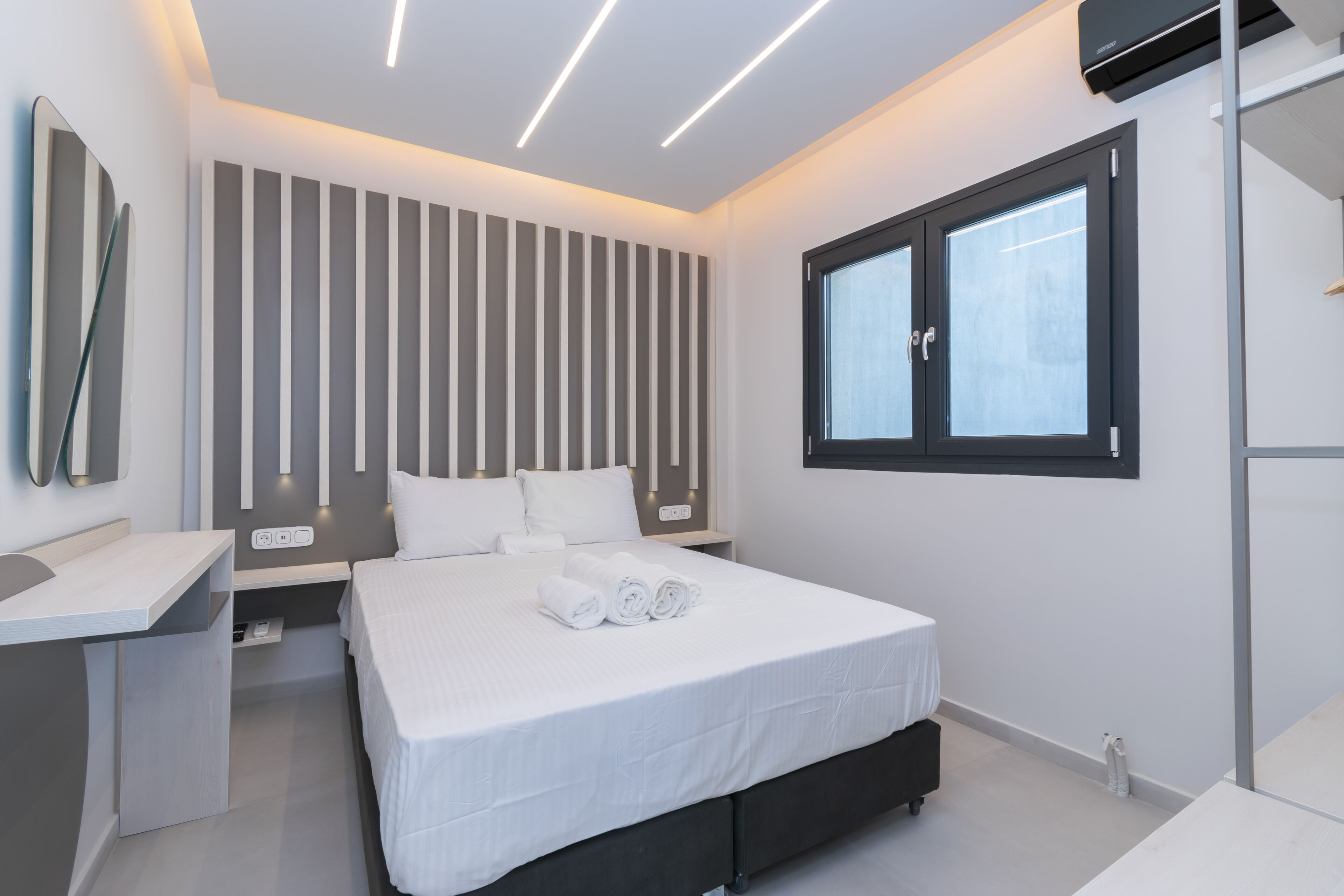 A modern bedroom with a large bed, bedside tables, a window, and a wall-mounted air conditioning unit.