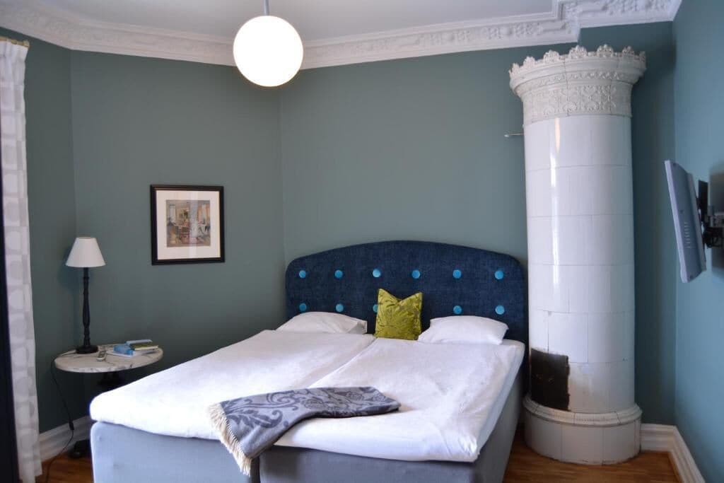 A bedroom with a bed, a nightstand, a lamp, a framed picture, and a decorative column.
