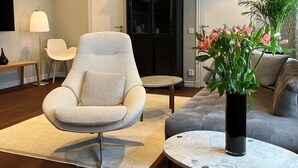 A modern living room with a grey armchair, a grey sofa, a round coffee table, and a black cabinet. - DA Hotel Apartments (Gothenburg)