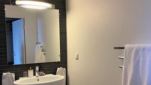 A modern bathroom with a large white sink, dark tiled walls, and a mirror above the sink. - DA Hotel Apartments (Gothenburg)