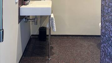 A bathroom with a white sink, a mirror, a towel hanging on a rack, and a shower area with a tiled floor.
