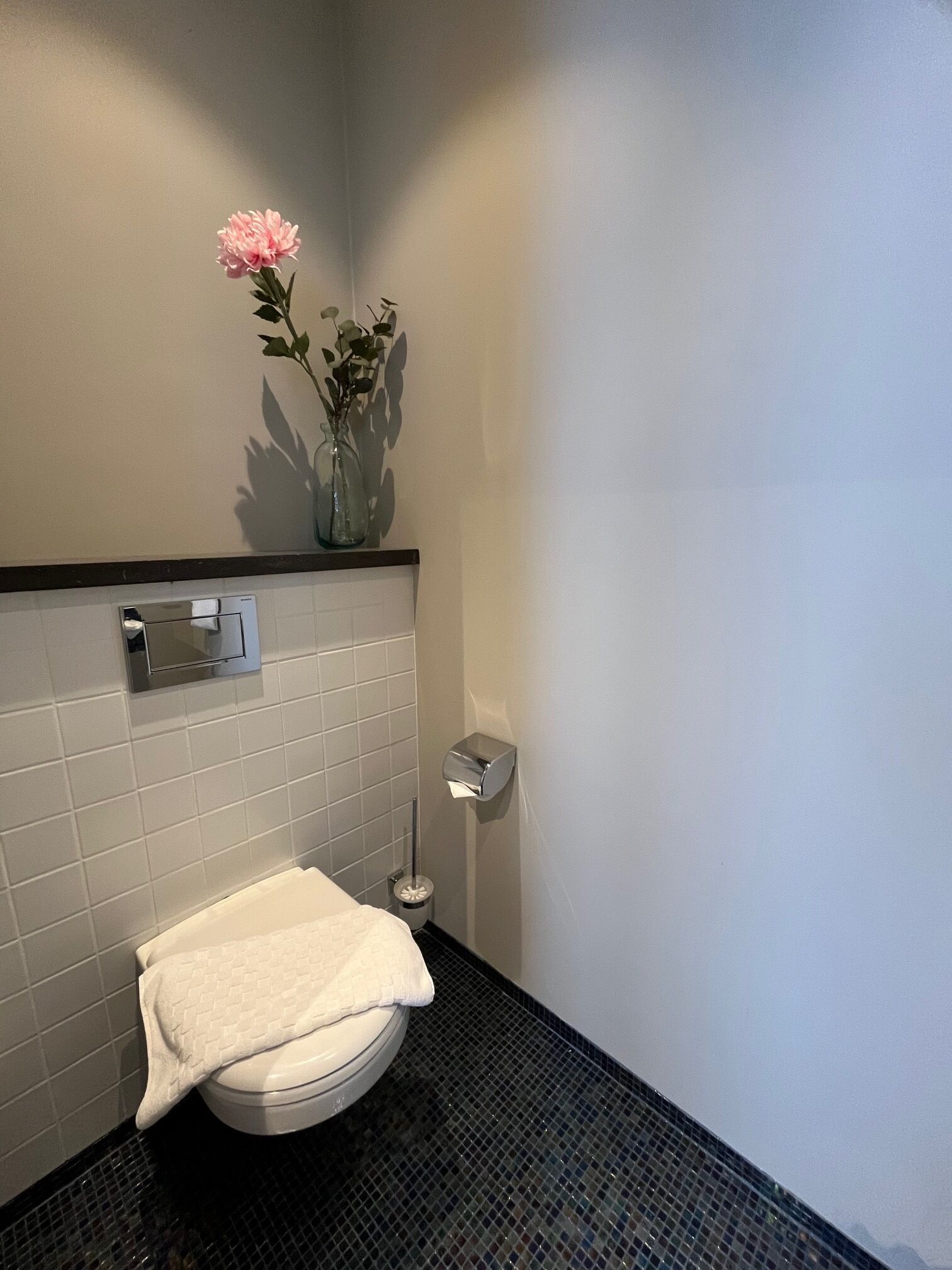 A bathroom with a toilet, a hand dryer, and a vase with flowers on the wall.