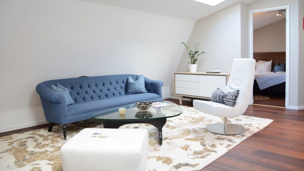 A modern living room with a blue sofa, a white armchair, a glass coffee table, and a white cabinet. - DA Hotel Apartments (Gothenburg)