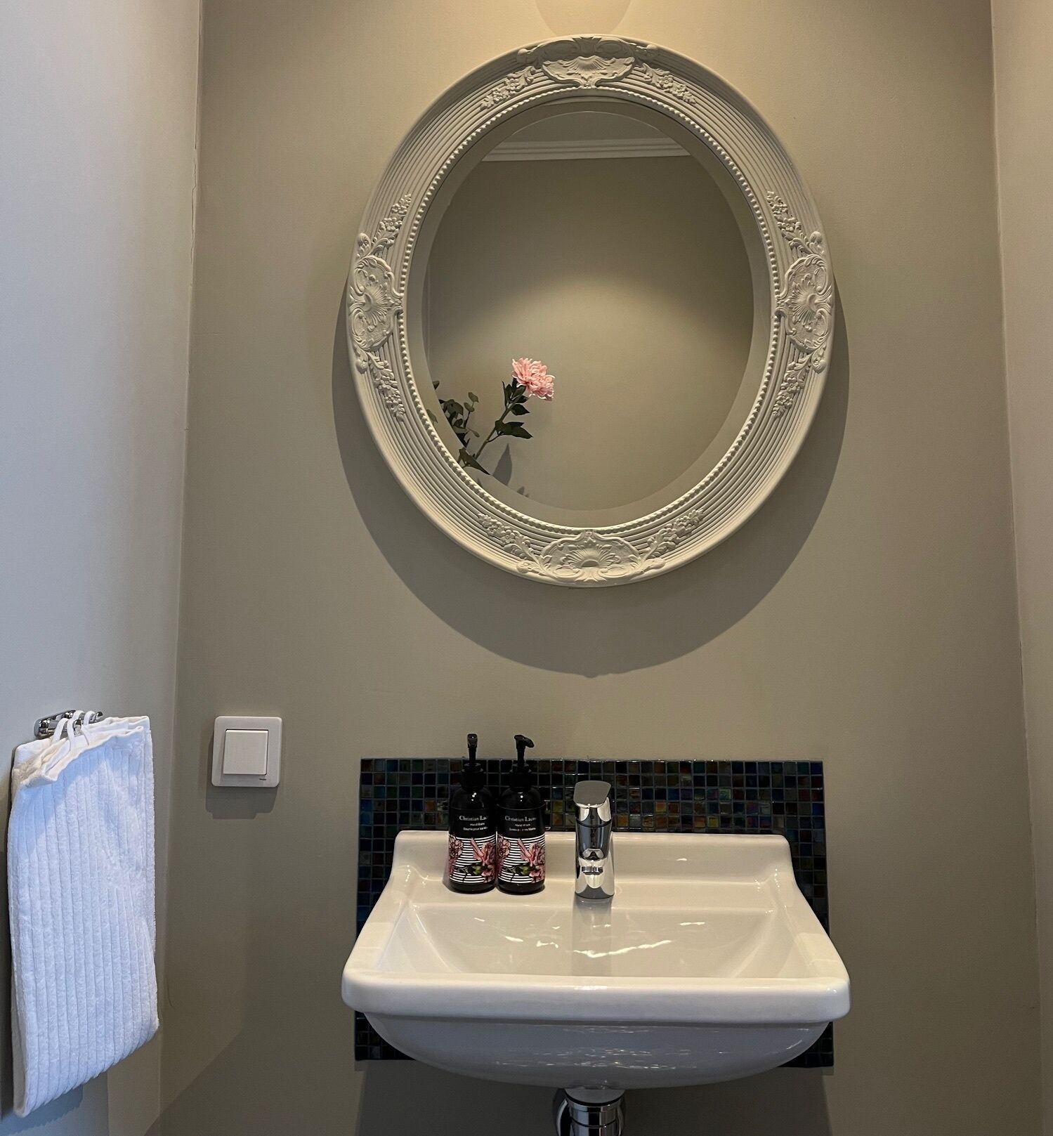Un baño con un espejo redondo, un lavabo blanco y un perchero para toallas.
