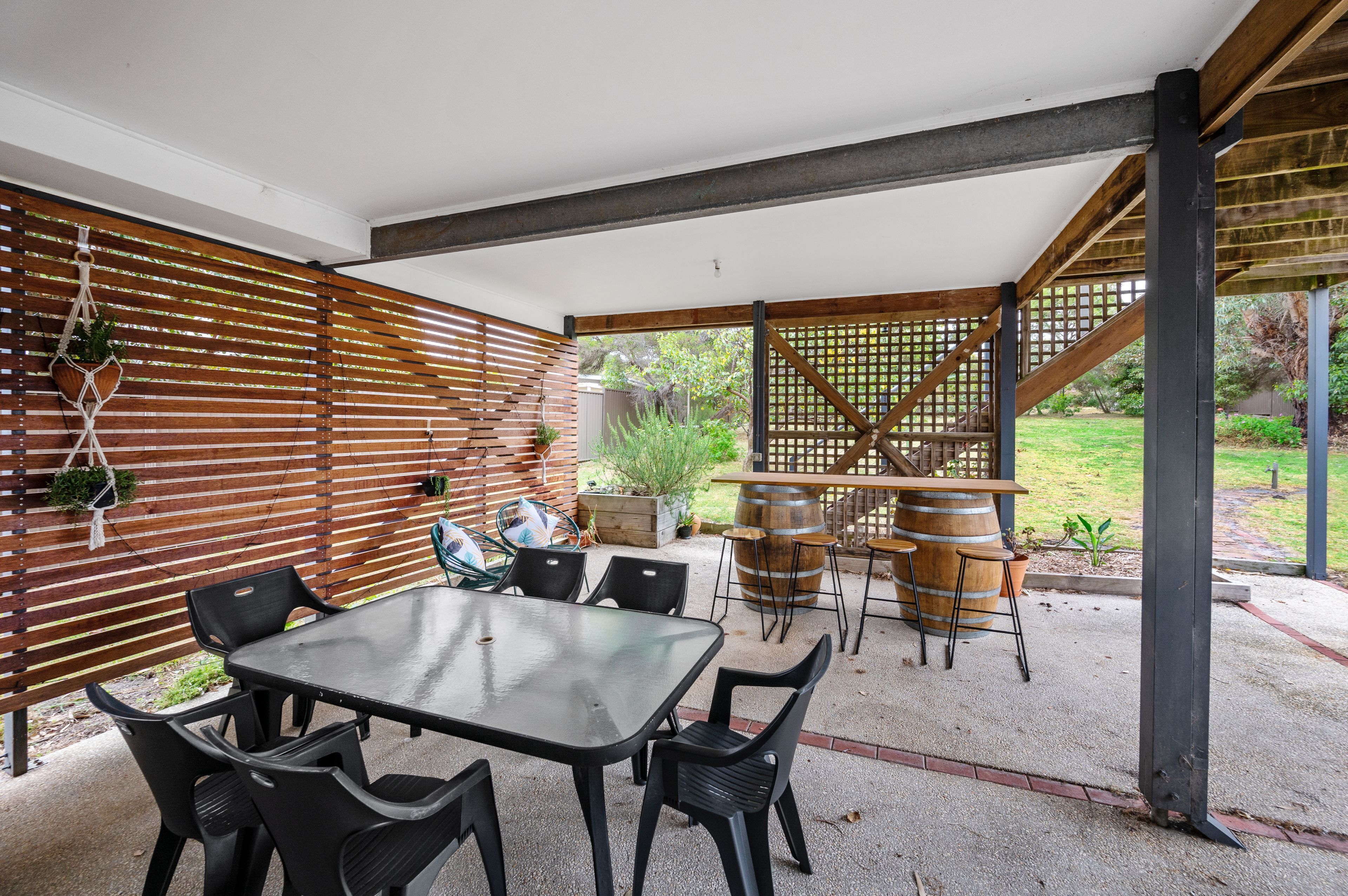 An outdoor patio with a table and chairs, wooden slats, and a trellis structure.