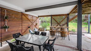Um pátio externo com mesa e cadeiras, ripas de madeira e uma estrutura de treliça.