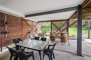 An outdoor patio with a table and chairs, wooden slats, and a trellis structure. - Three Beaches (Anglesea)