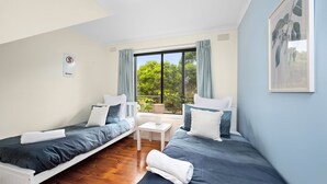 A room with two beds, a small table, a window with curtains, and a sign on the wall. - Three Beaches (Anglesea)