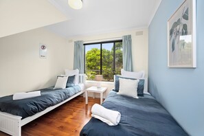A room with two beds, a small table, a window with curtains, and a sign on the wall. - Three Beaches (Anglesea)