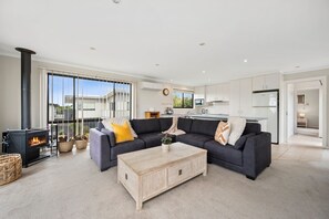 A modern living room with a fireplace, a sofa set, and a kitchen in the background.